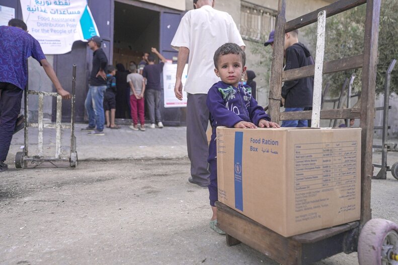 A young child standing next to a food box provided by WFP. © WFP/Ali Jadallah