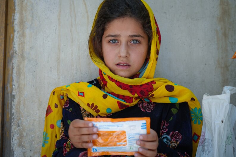 Une fillette tenant devant la caméra un paquet de pâte d'arachide enrichie destinée à lutter contre la malnutrition. © PAM/Mohammad Hasib Hazinyar