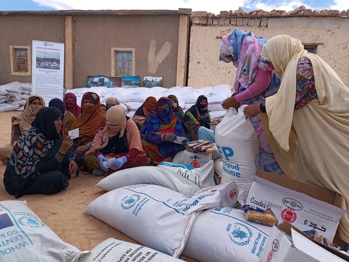 Les femmes réfugiées sahraouies s'assoient en groupe pour distribuer les rations alimentaires mensuelles, en se protégeant toujours la tête et le visage du dur soleil du désert.