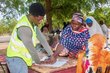 A woman in a colourful headscarf and shawl signs with her fingerprint on a register to receive WFP food aid. Photo: WFP/Joseph Fambove