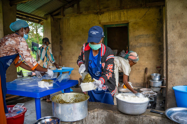 Photo: PAM/Michael Castofas. Portant des masques, des gants et des tabliers, Kahindo Anita et son équipe préparent et emballent des repas chauds à base de riz et de feuilles de manioc destinés aux patients d’un centre de traitement d’Ebola à Oicha. Le PAM soutient la préparation de repas nutritifs dans le respect des normes de sécurité alimentaire.