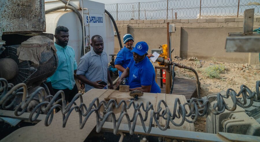 Men examine the back of a truck, there is a connecting wire in the foreground
