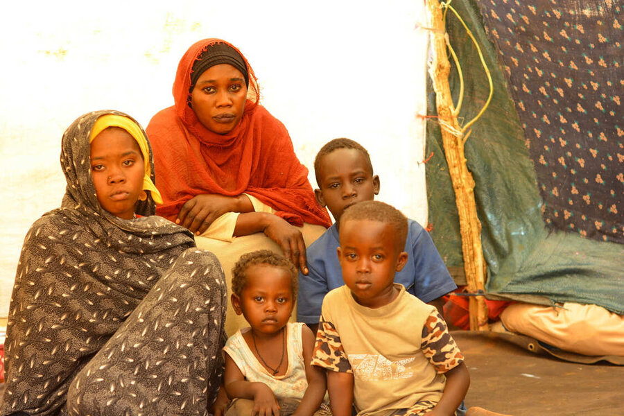 A Sudanese woman in dark orange Islamic dress with a girl in a hijab and 3 boys