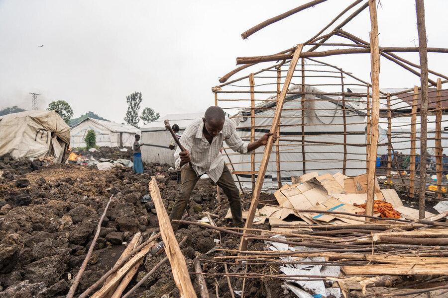 A man dismantles the wooden frame of a tarpaulin shelter in a camp