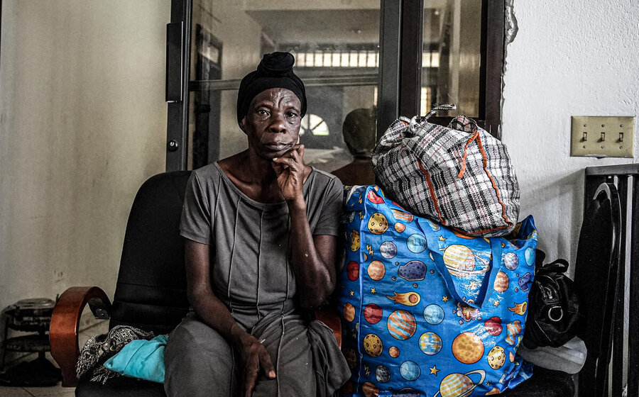 A displaced woman in Haiti with a bright blue PVC bag next to her look contemplative