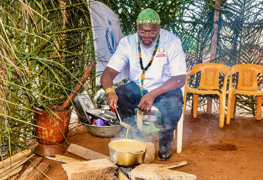 A man in a white T-shirt and beaded cap stirs a pot over an open fire. Photo: WFP/Jordan Onana