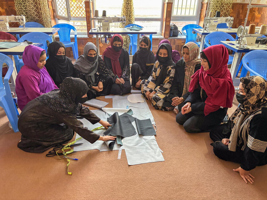 Women in long robes and headscarves are gathered in a circle as one of them lays out fabric. Photo: WFP/Simon Renk
