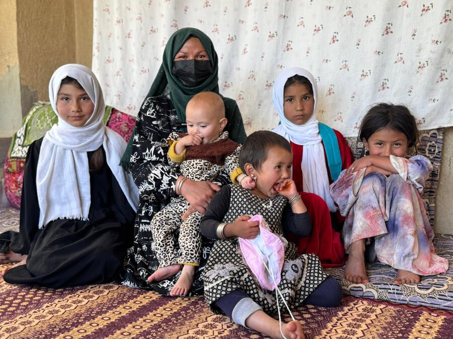 A woman in a face-covering headscarf and long robe sits on a rug surrounded by her small children. Photo: Danijela Milic