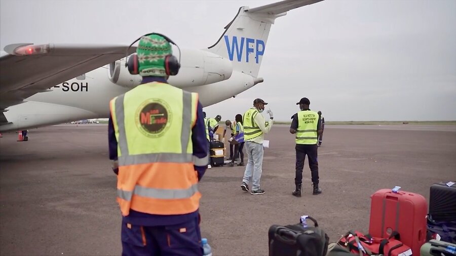 A WFP UNHAS plane sits on the airport tarmac, as passengers disembark and airport workers unload bags. Photo: WFP