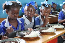 Photo : PAM/Alexis Masciarelli. Des élèves âgés de 5 à 7 ans prennent un repas chaud dans leur classe de l'école primaire Baptiste Salem de Dondon, qui compte 600 élèves. Les repas sont préparés quotidiennement à partir de riz et de haricots achetés à des producteurs locaux, dans le cadre du programme d'alimentation scolaire à base de produits locaux du PAM. 