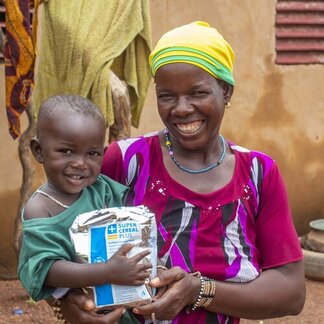 Un enfant assis sur les genoux de sa mère tient un paquet de céréales du PAM.