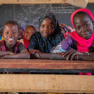 Trois enfants face à la caméra dans un bureau d'école
