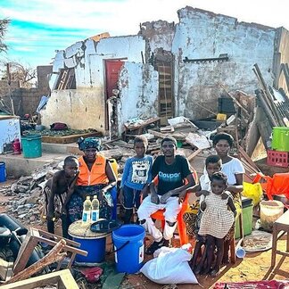 Un groupe de sept adultes et enfants sont debout et assis devant un bâtiment en ruine.